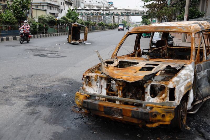 A man rides his motorbike on a mostly empty street past vehicles that were set on fire during clashes among university students, police and government supporters, after violence erupted during what were initially protests against government job quotas,Dhaka, July 22, 2024. (Mohammad Ponir Hossain/Reuters)